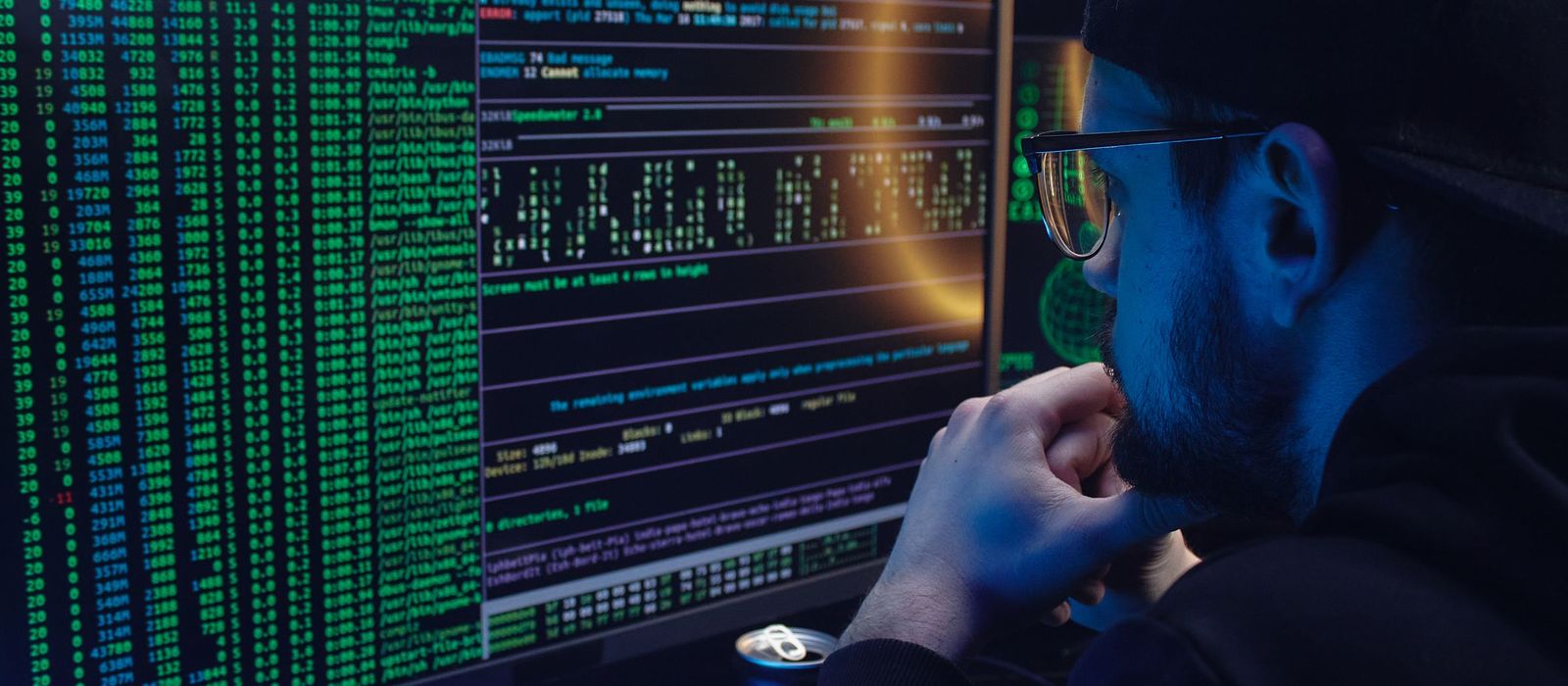 Dark monitors showing server logs and terminal output, an engineer out of focus at the side